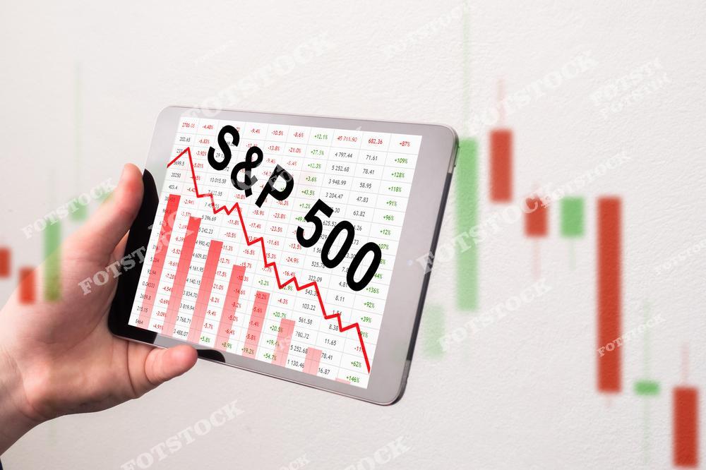 На изображении планшет с отображением графика падения индекса S&amp;P 500 и таблицы финансовых данных. На фоне видны размытые свечные графики, подчеркивающие тему анализа фондового рынка. Снимок символизирует волатильность рынков, инвестиции и мониторинг финансовых показателей.